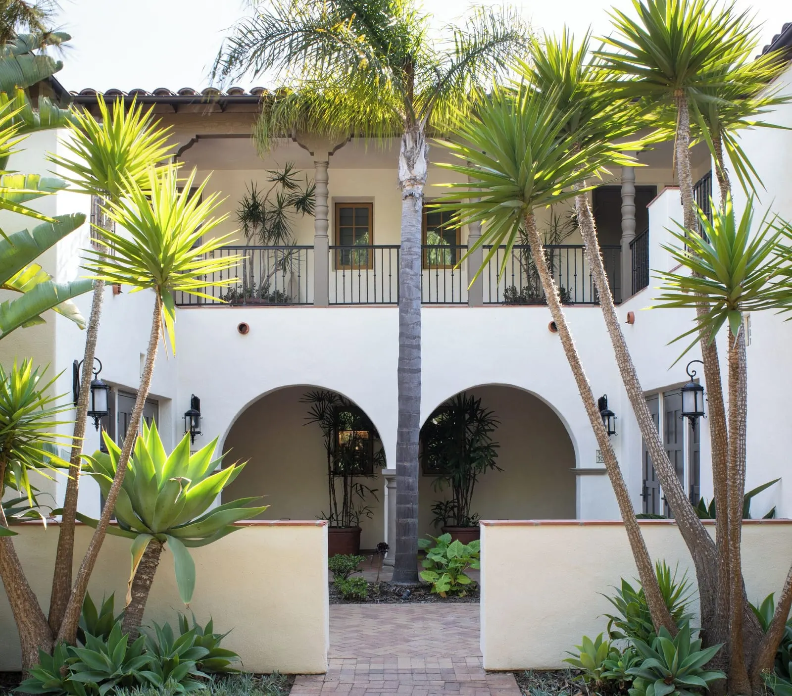 Bungalow King Guestroom at Terranea Resort: a courtyard of white buildings with arched ground-floor openings under an upper balcony, framed by palms and agave
