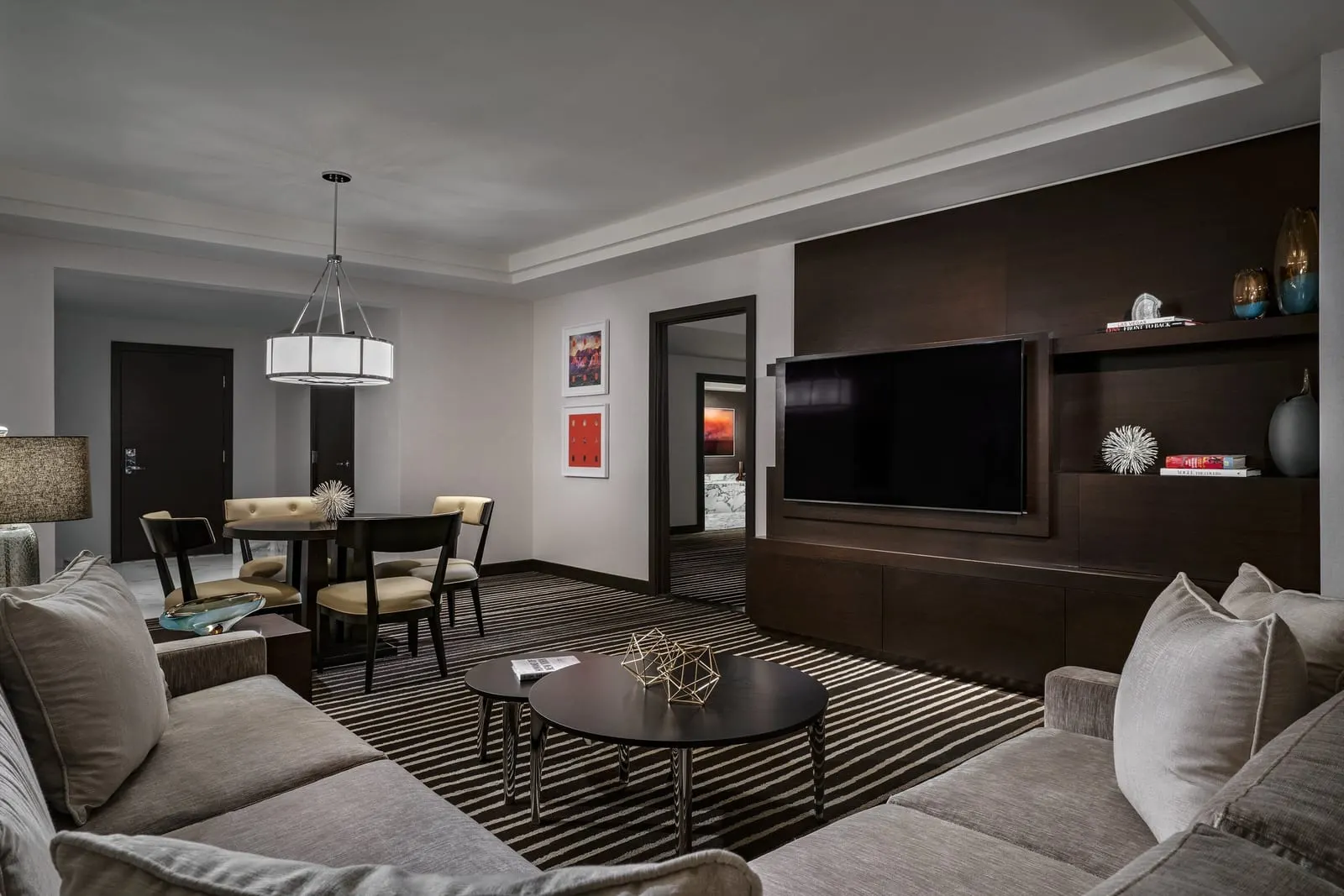 Signature Suite King at Red Rock Casino Resort & Spa: the living room, with two sofas around a pair of round coffee tables, a dining table with four chairs under a pendant light and a television set into a dark wood wall unit