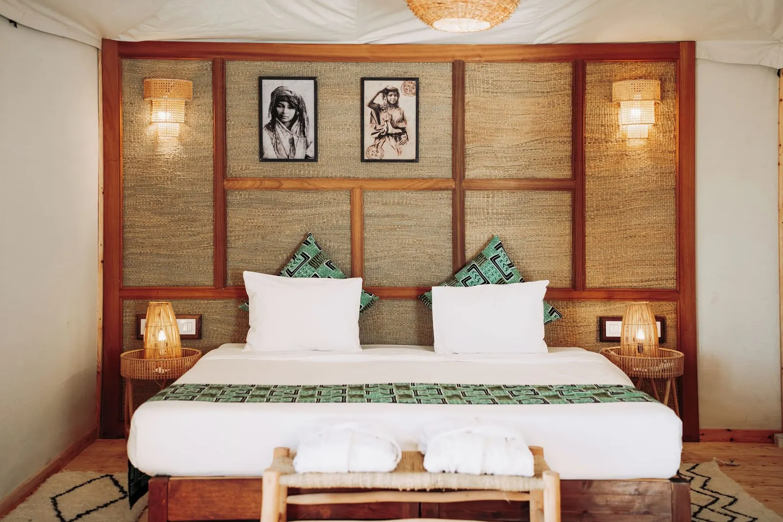 Emotion Suite at Inara Camp: a king-size bed with white linen and green cushions against a woven headboard hung with two framed photographs.