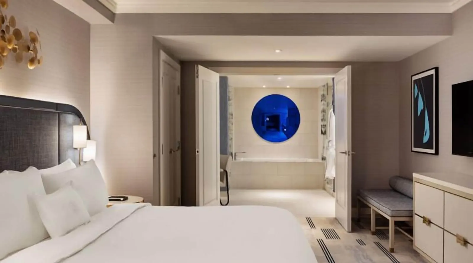 Royal Suite Pool View at Fontainebleau Las Vegas: the king bedroom, with double doors open onto a bathroom with a bathtub under a round blue mirror