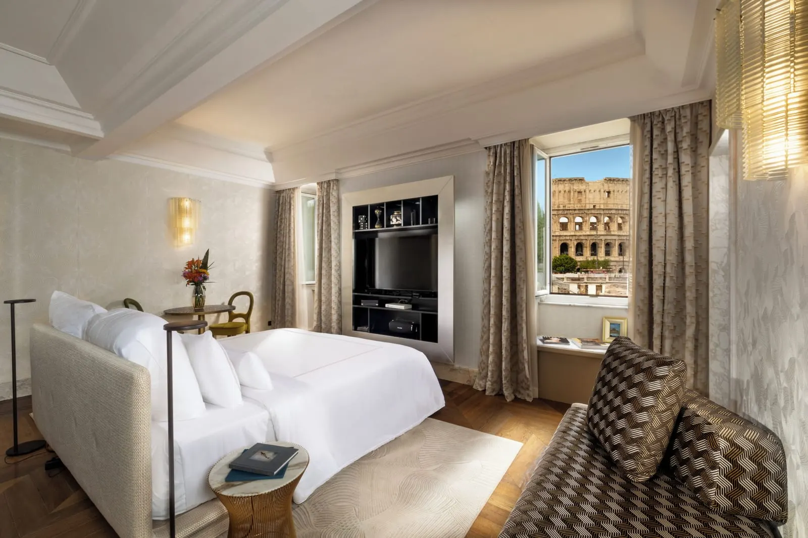 Ludus Magnus Suite at Palazzo Manfredi: the bed, a sofa and a TV wall, with the Colosseum in the window
