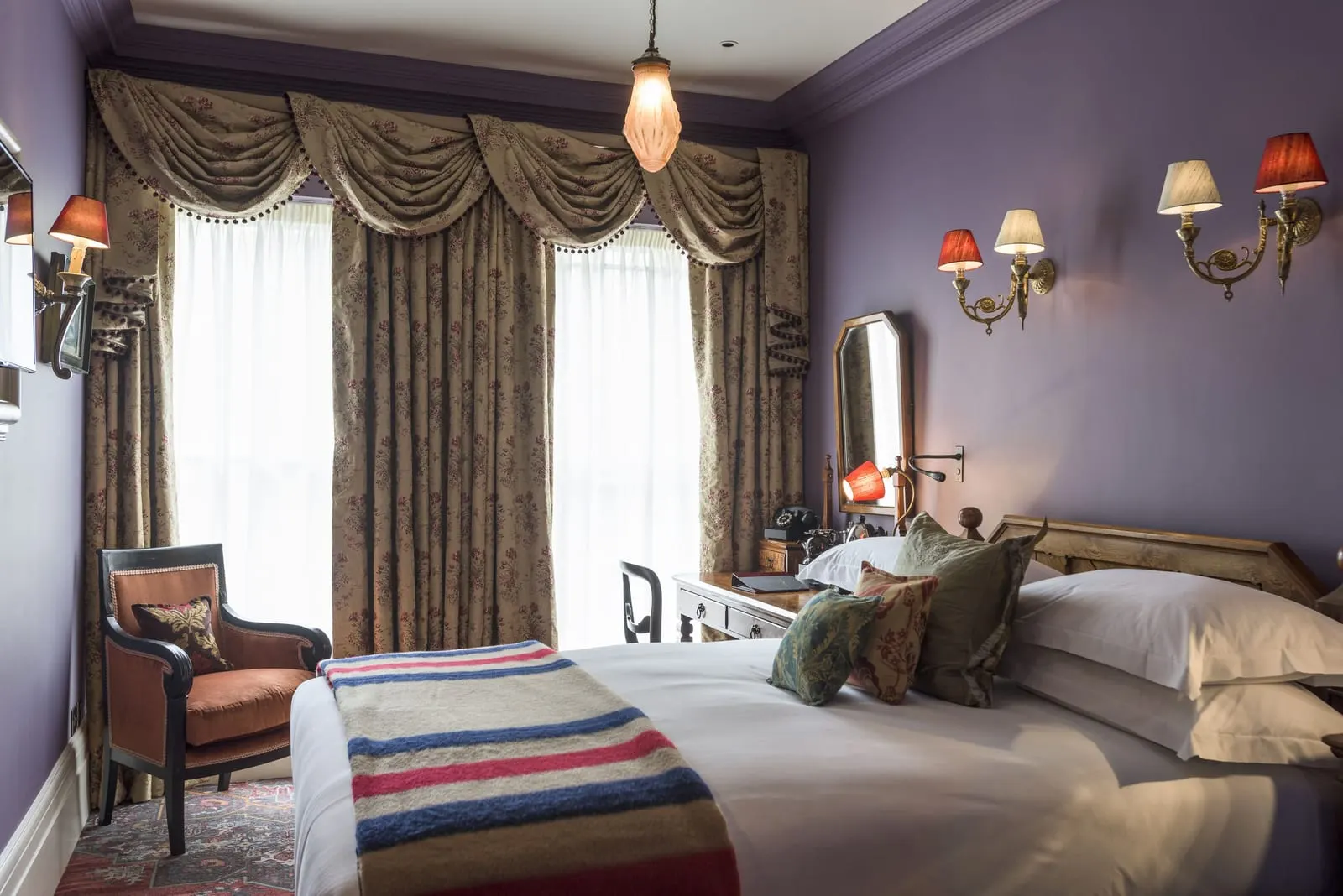 Deluxe Double at The Zetter Marylebone: the bed with a striped blanket, lilac walls, swagged curtains and an armchair