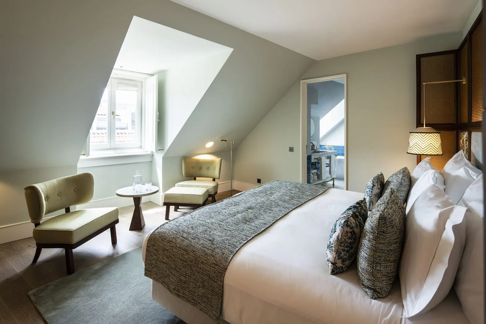 Superior Room at Palácio Ludovice: the bed under a sloping ceiling with a dormer window, two armchairs and a side table