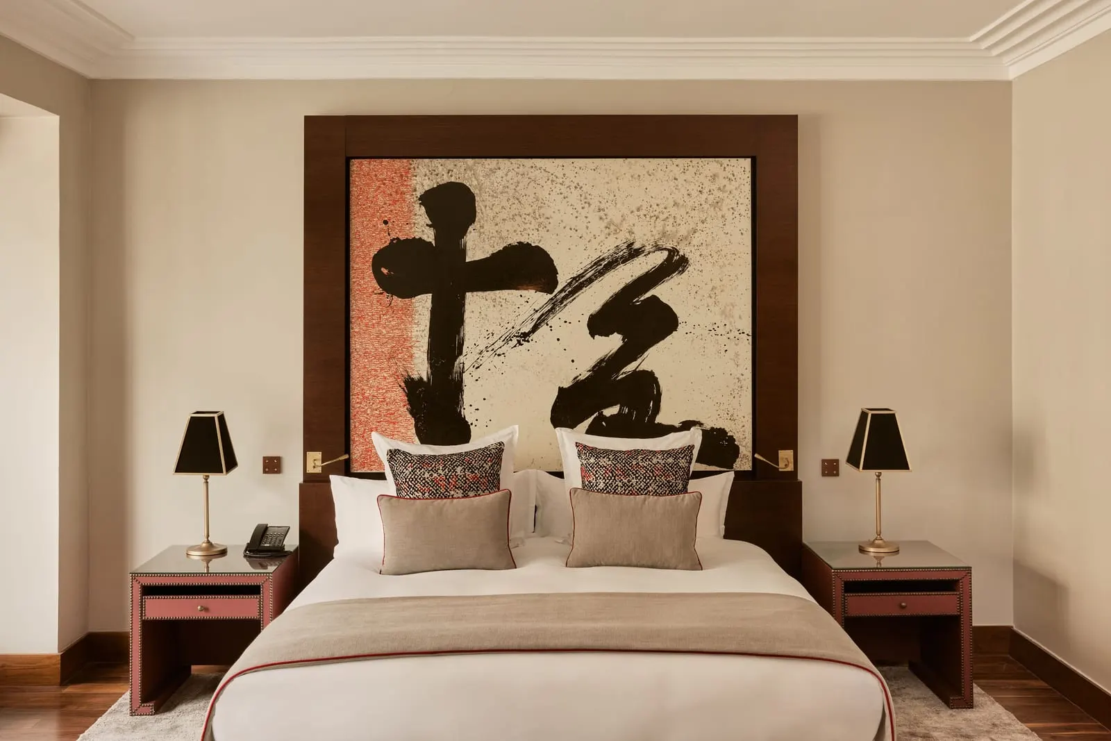 Deluxe Junior Suite at Nobu Hotel Marrakech: a king bed with red and cream cushions beneath a large calligraphy panel, flanked by bedside lamps