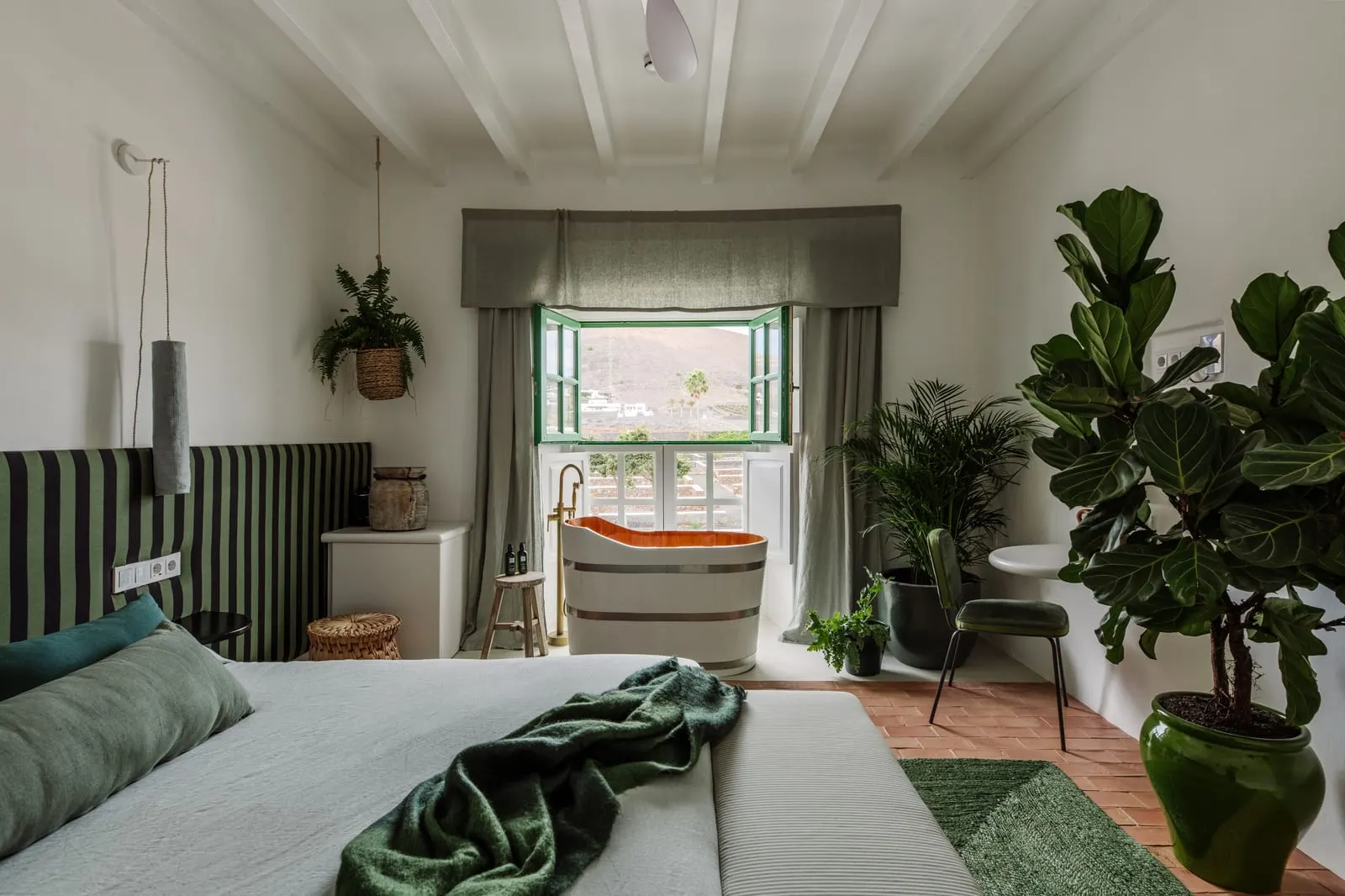 Double Room with Volcano View à l'Hotel César Lanzarote : une chambre avec une baignoire îlot près d'une petite fenêtre et une tête de lit rayée
