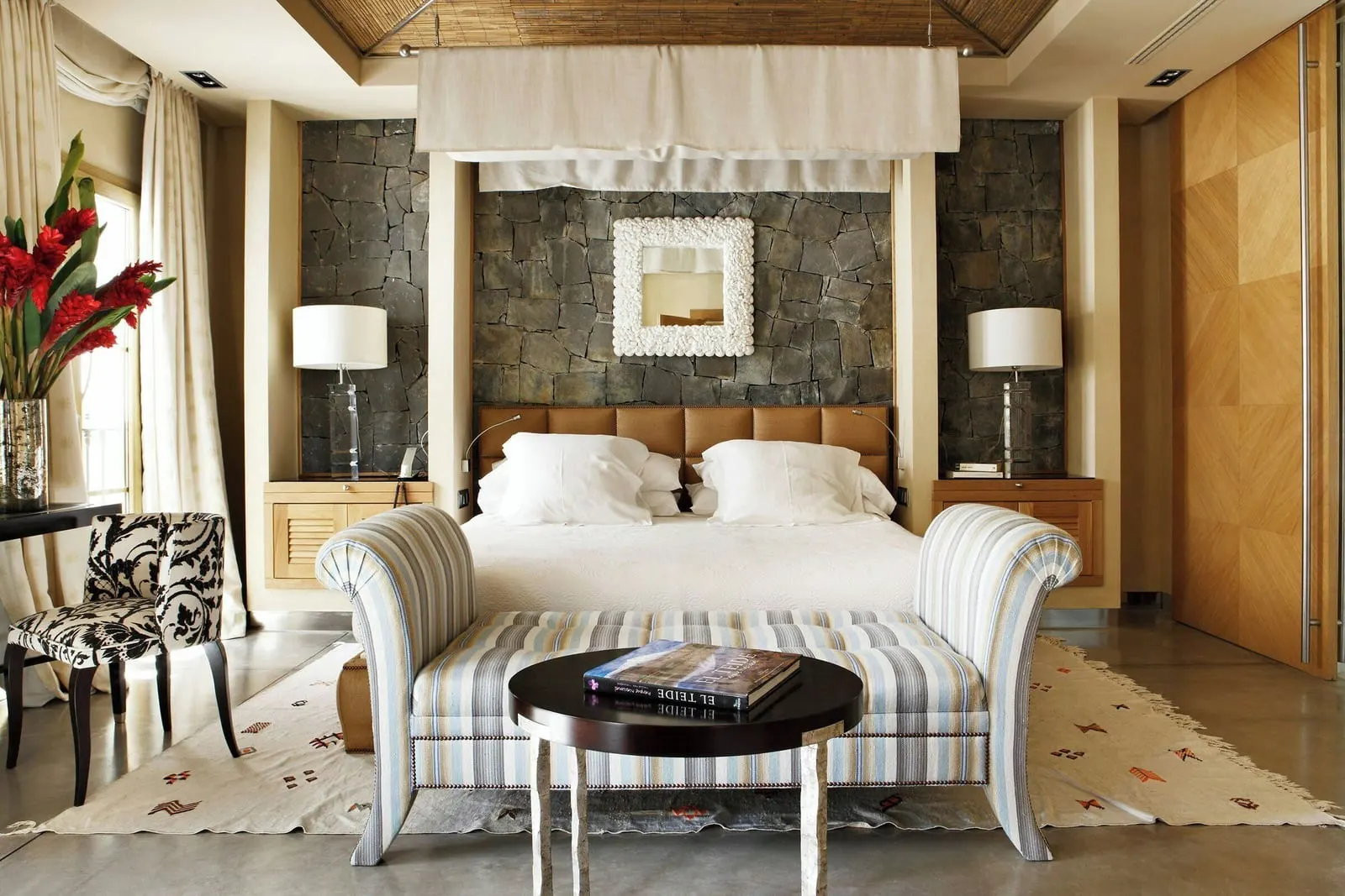 Villa Las Mimosas at Bahía del Duque: a canopy bed against a dark stone wall, with a striped bench at its foot