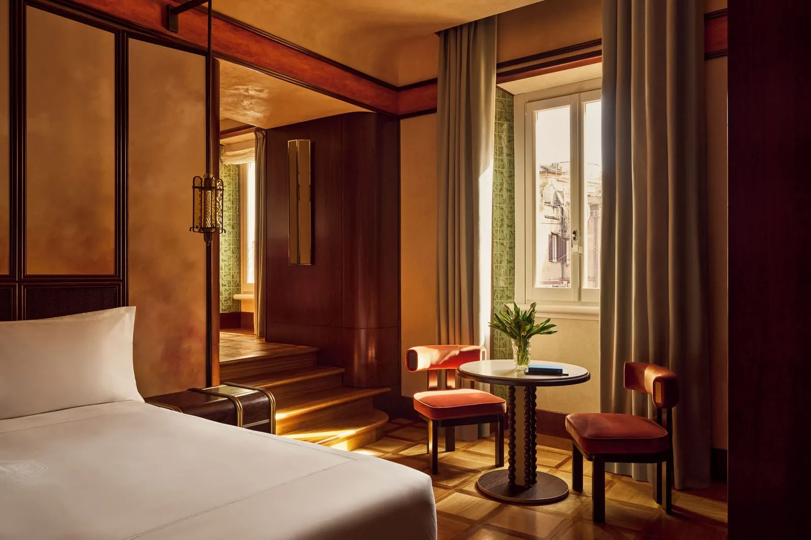 Deluxe Room at Orient Express La Minerva: the bed, a small table with two chairs by the window and steps to a raised alcove