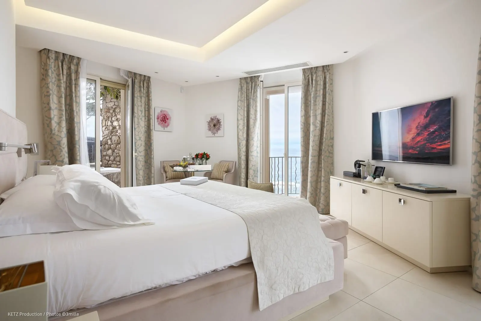 Le Parc Junior Suite 510 at Cap Estel: the bed facing a wall-mounted television, with windows on two sides