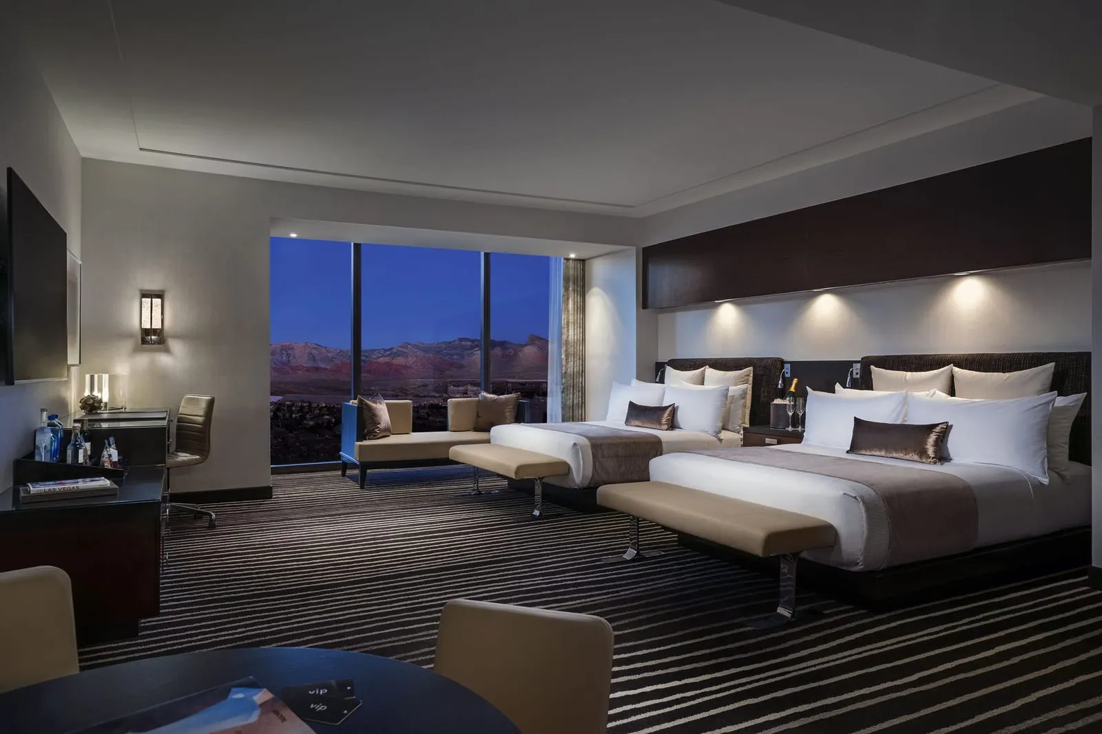 Executive Two Queens Corner Room at Red Rock Casino Resort & Spa: two queen beds with an upholstered bench at the foot of each, a small sofa by a floor-to-ceiling window, a desk on the left and a round table with chairs in the foreground