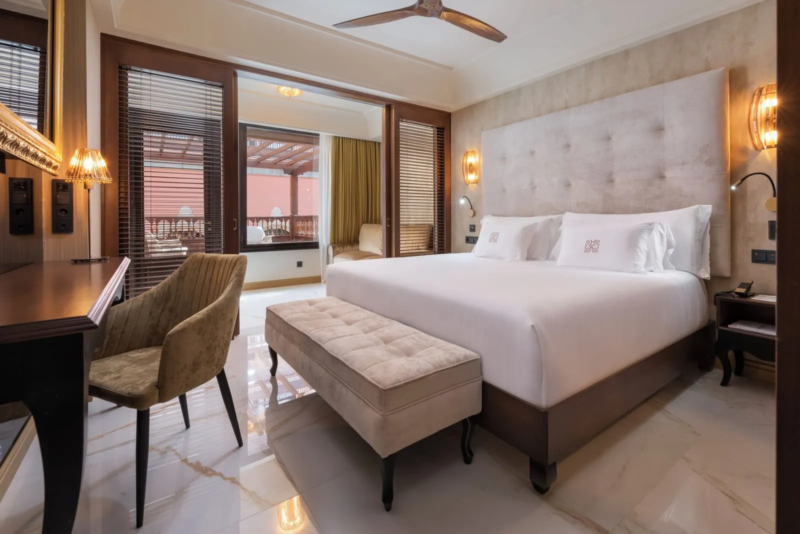 Family Deluxe at Santa Catalina, a Royal Hideaway Hotel: a king bed with a padded headboard and a bench at its foot, a desk, and sliding doors open to a sitting area and a terrace