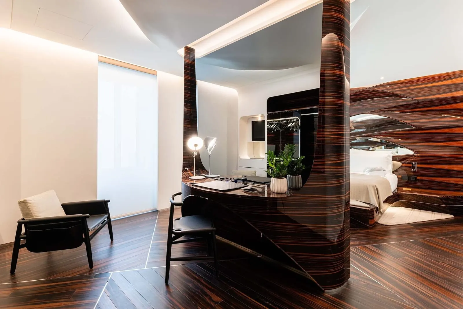 Grand Suite with Roof Garden at ROMEO Roma: an armchair and a desk wrapped round an ebony column, the bed beyond