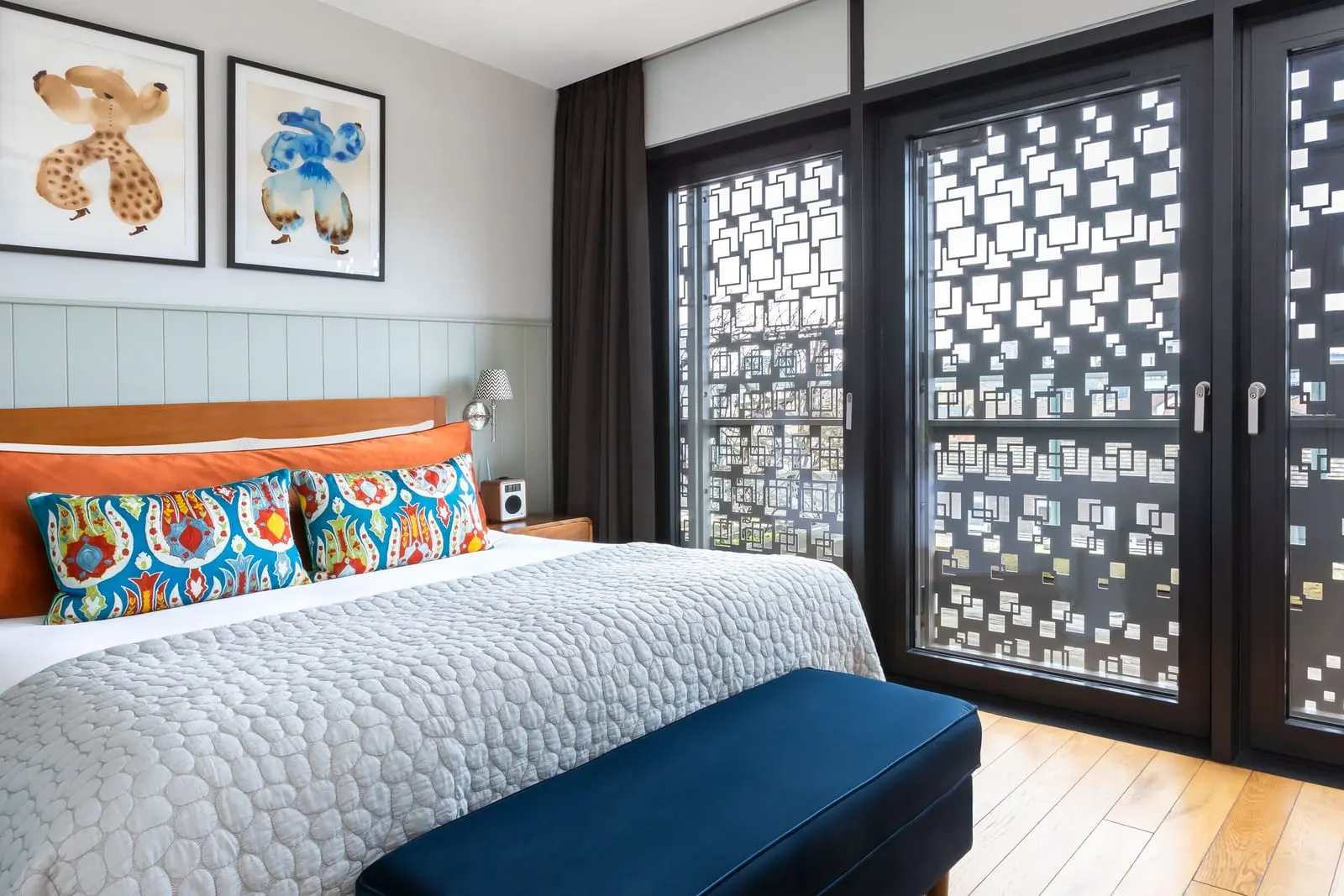 Deluxe One Bedroom Suite at Town Hall Hotel: the bed with patterned cushions beside tall windows with patterned metal screens