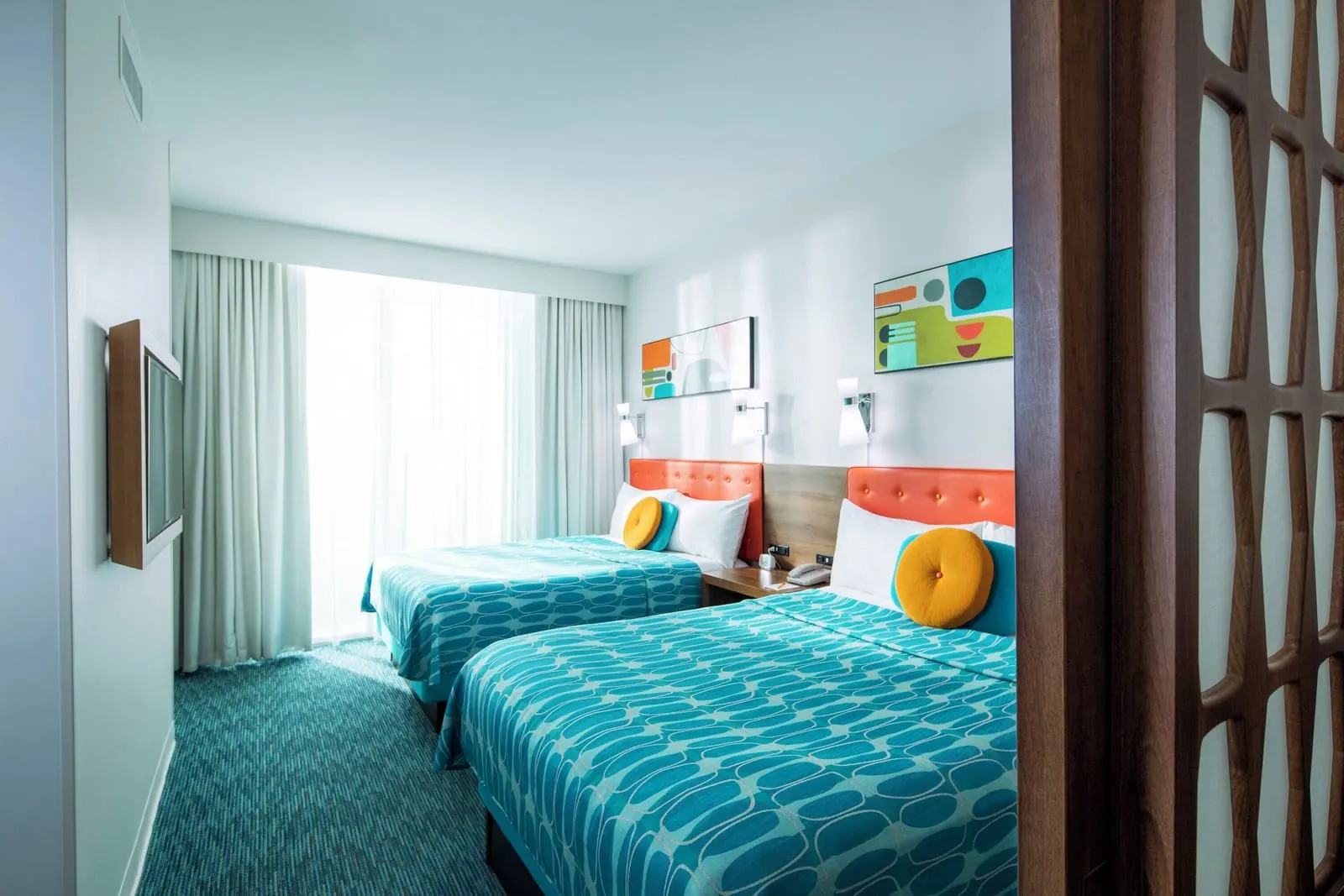Poolside Family Suite Interior Entry at Universal Cabana Bay Beach Resort: the bedroom seen past the sliding lattice partition, with two queen beds, a wall-mounted television and a wide window with sheer curtains