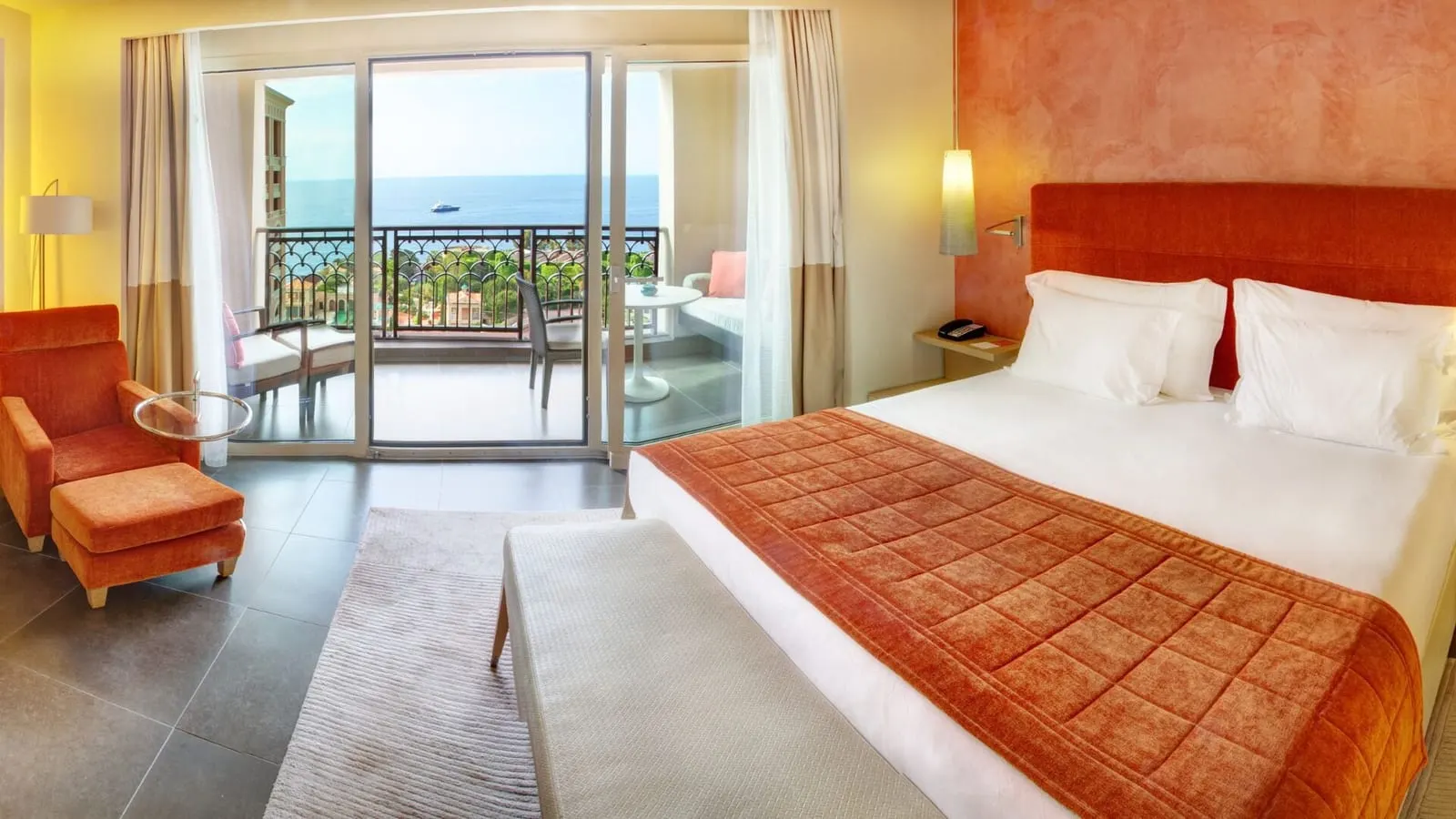 Exclusive Room with sea view at Monte-Carlo Bay Hotel & Resort: the bed, an orange armchair and glass doors to the terrace and the sea