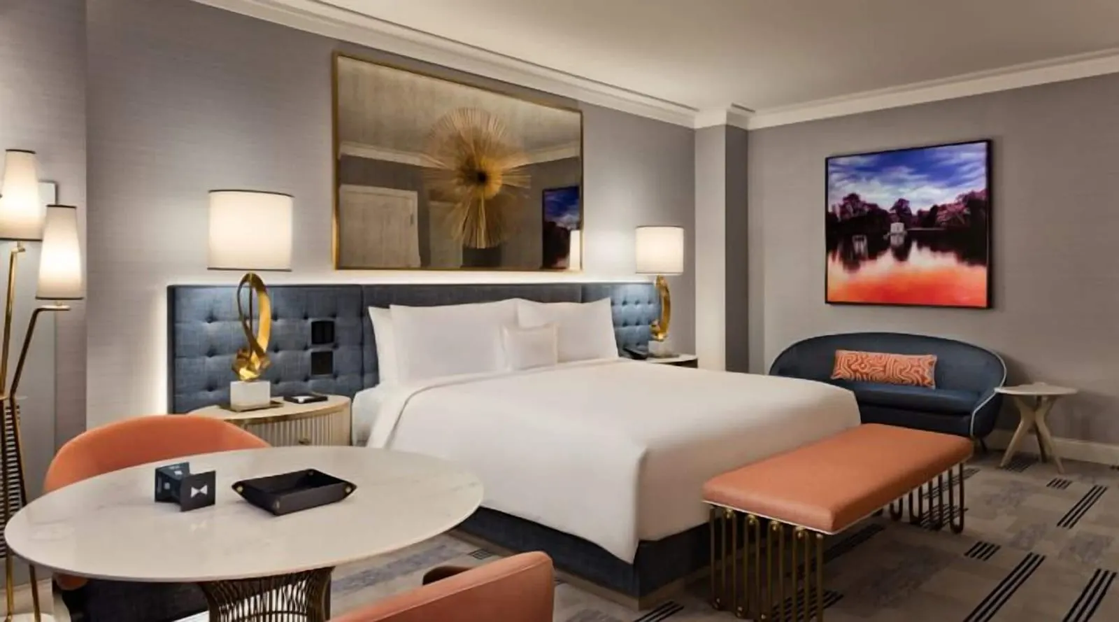Bleau King at Fontainebleau Las Vegas: a king bed against a tufted blue headboard under a gilt-framed mirror with a gold starburst, a peach bench at its foot, a navy loveseat and a round marble table with two chairs