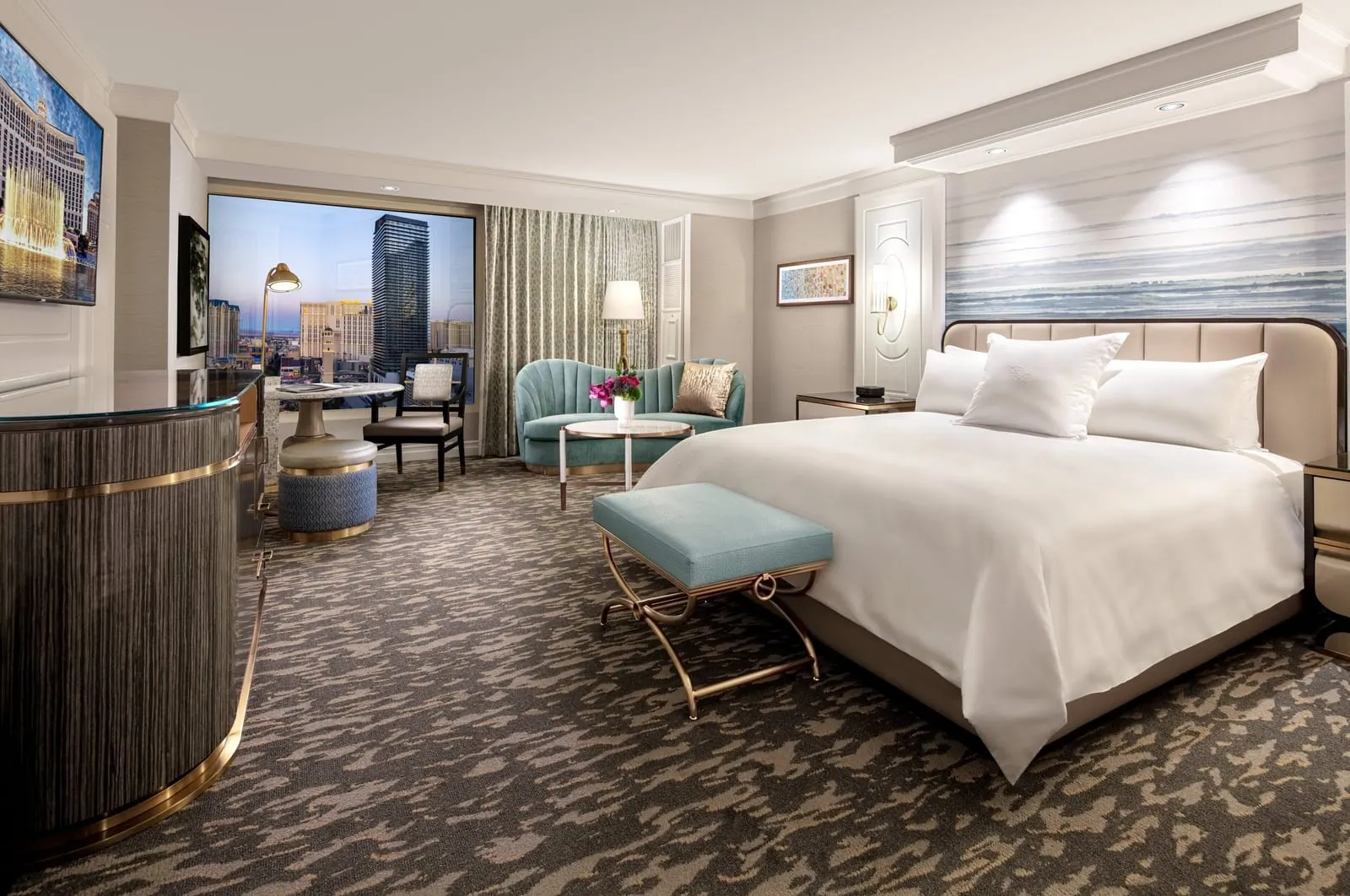 Strip View Spa King at Bellagio: a king bed, a teal loveseat and a round table, with a window looking onto hotel towers on the Strip
