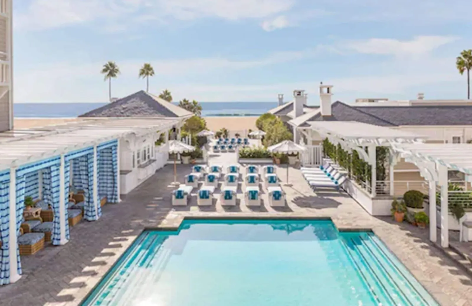 Ocean View Room im Shutters on the Beach: der Pool von oben gesehen, mit blau gestreiften Cabanas und weißen Liegen, und dem Strand und dem Meer hinter den niedrigen Dächern