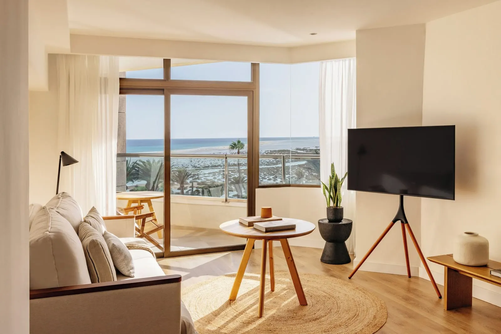 The Reserve Junior Suite Ocean Front at Paradisus by Meliá Fuerteventura: a sitting area with a sofa, a round table and a television, by a corner of glass doors to a balcony over the sea