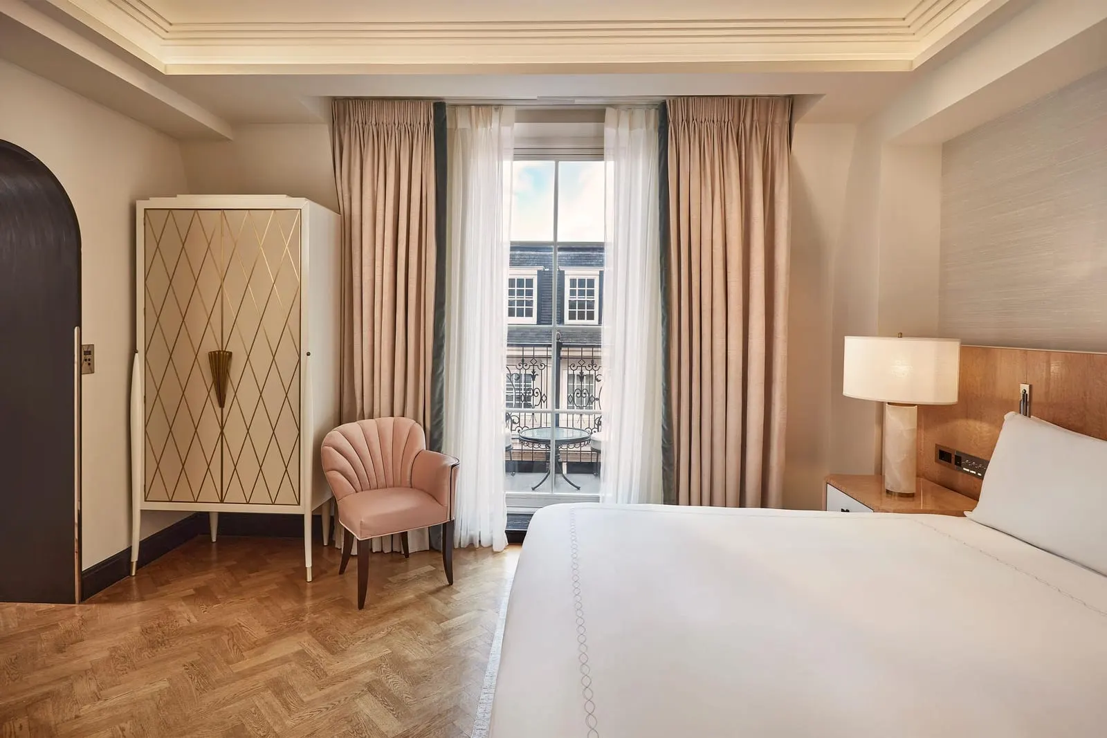Mayfair Balcony Room at Claridge's: the bed, a pink armchair, a patterned wardrobe and a tall window onto the balcony