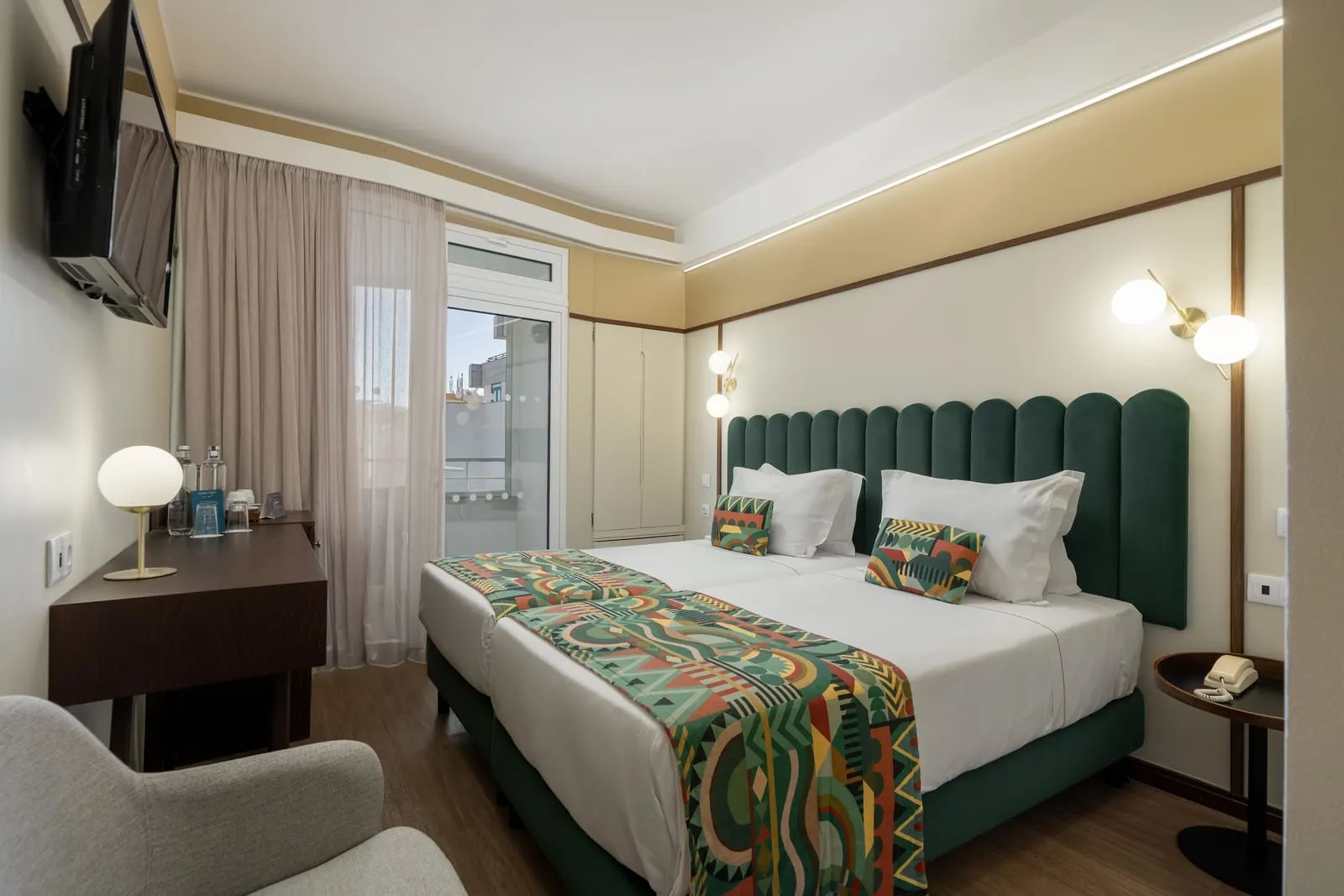 Standard Balcony Room im Hotel Madeira: zwei Einzelbetten mit gemusterten Überwürfen unter einem grünen gepolsterten Kopfteil, mit einer Tür hinaus auf den Balkon