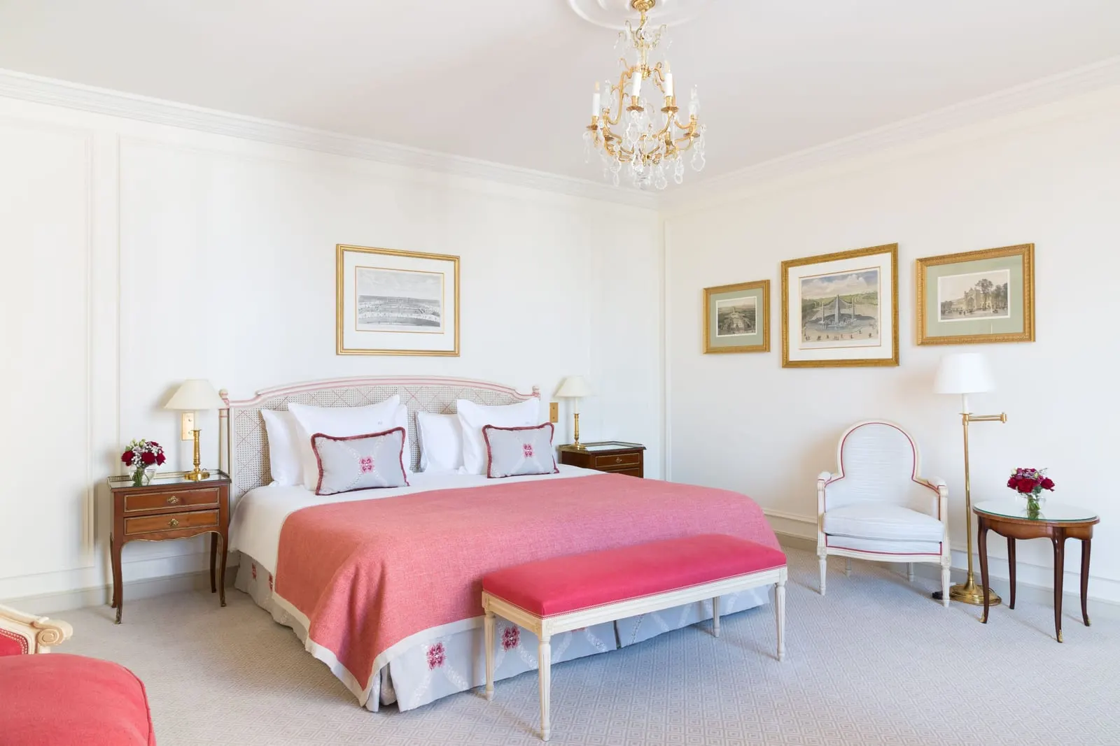 Suite Penthouse at Le Bristol Paris: a bed with a pink throw and a pink bench, with a group of framed prints above an armchair and a side table