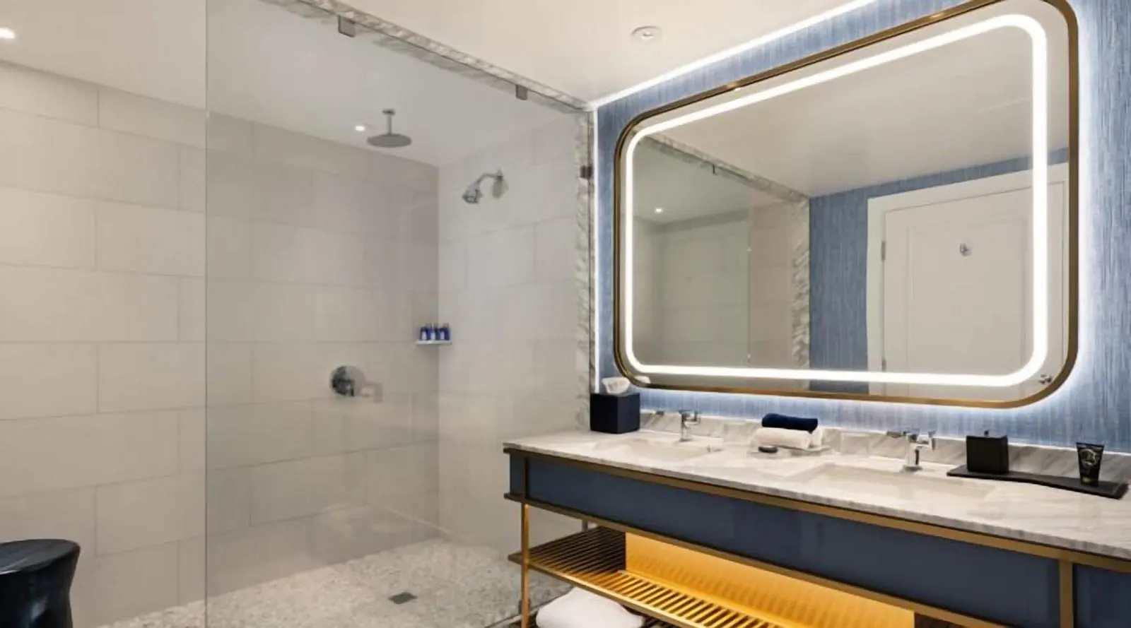 Gold King Strip Best View at Fontainebleau Las Vegas: the bathroom, with a walk-in shower behind a glass panel and two basins in a marble counter under a lit mirror