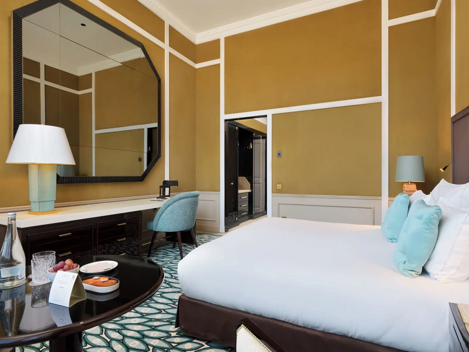 Grand Deluxe City Views room at The One Monumental Palace: the bed, a desk under an octagonal mirror and a welcome tray
