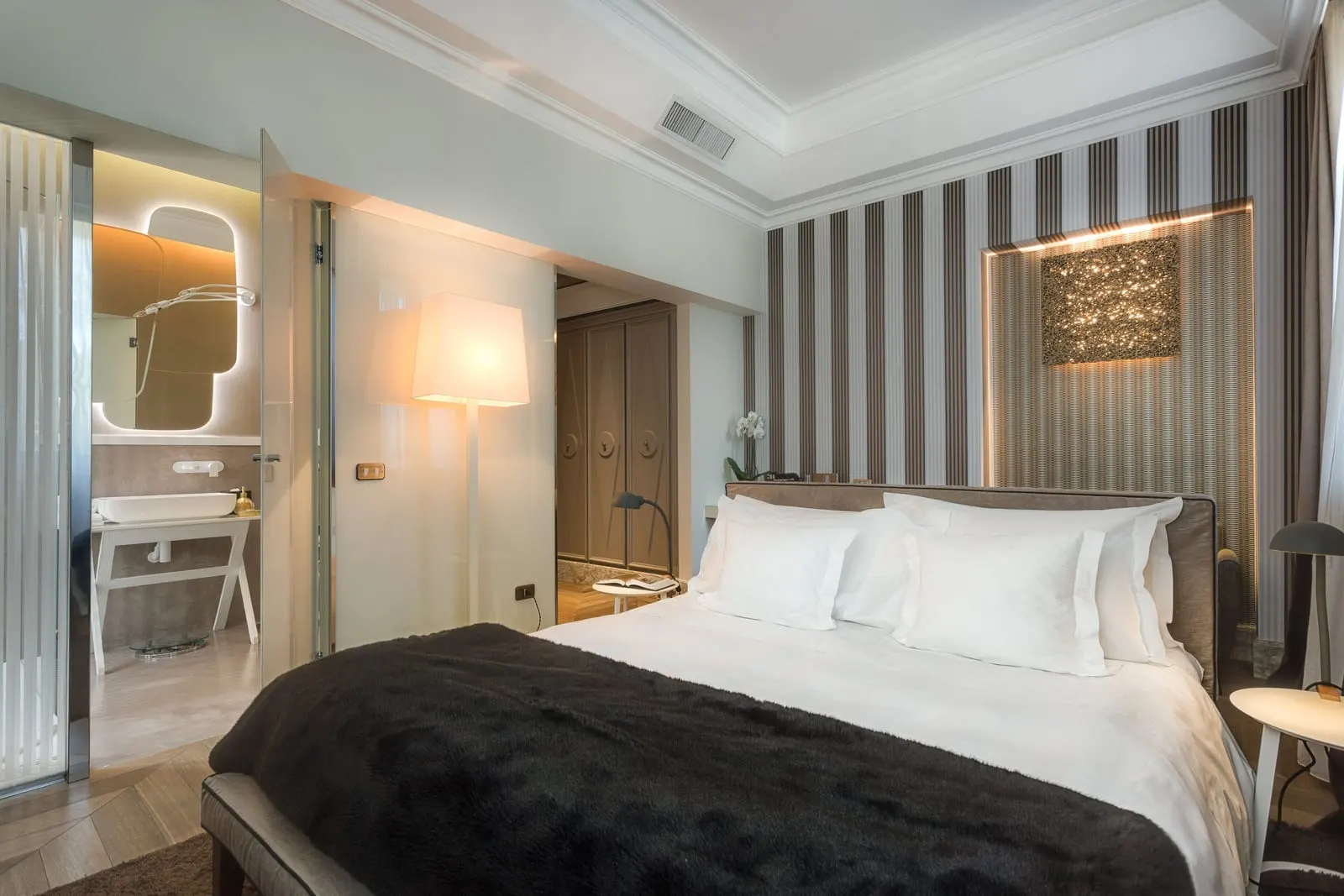 Executive Room at Palazzo Manfredi: a double bed against striped walls, with the bathroom door open on the left