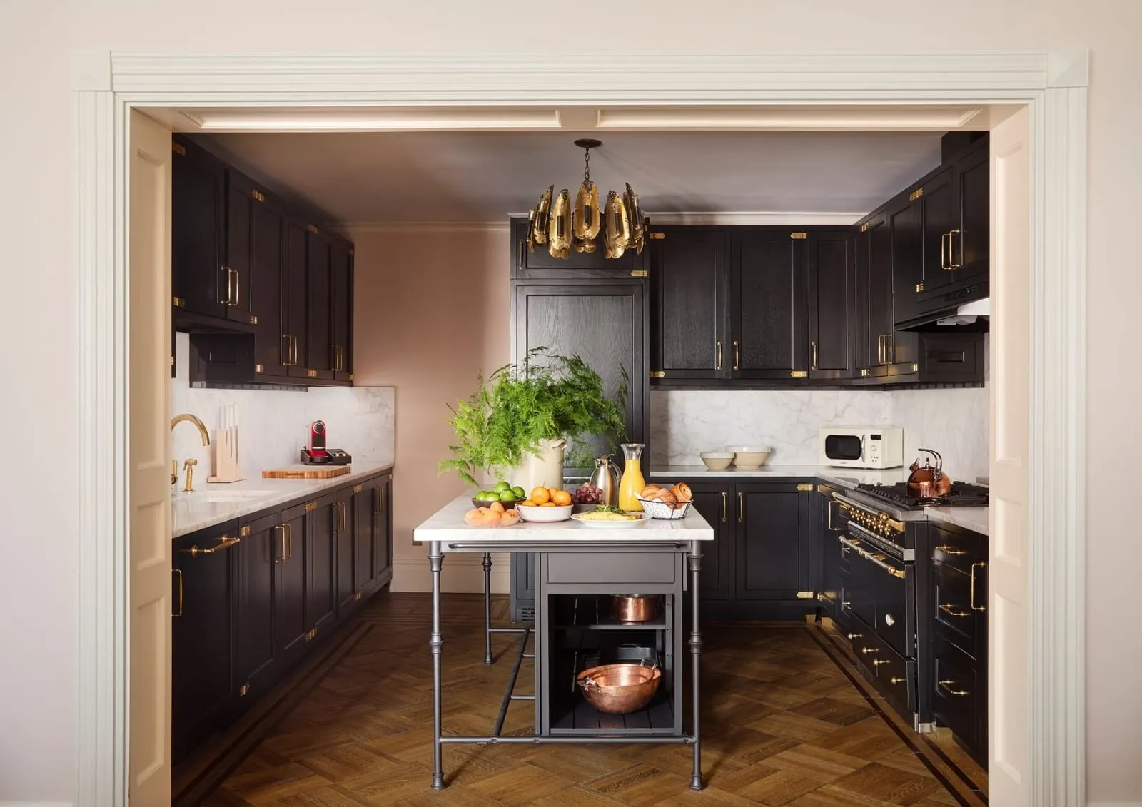 Two Bedroom Suite at Hotel Chelsea: a kitchen with black cabinets and brass handles, a freestanding range and a marble-topped island with fruit and pastries on it