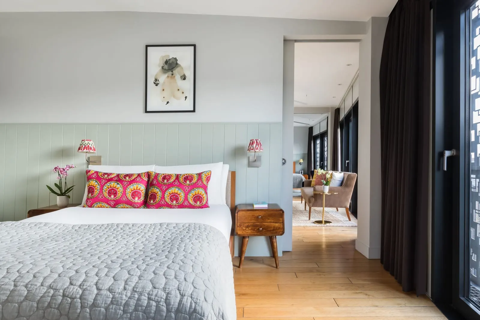 Deluxe Two Bedroom Suite at Town Hall Hotel: a bed with pink patterned cushions and a doorway through to a sitting area