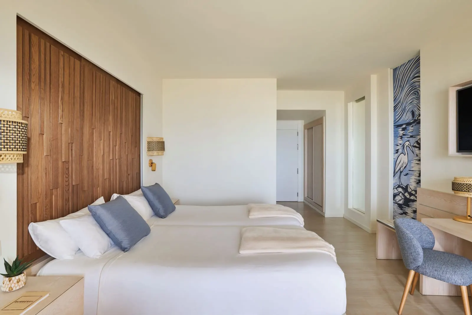 Sea-View Double at Iberostar Selection Fuerteventura Palace: two single beds against a slatted wooden headboard, with a desk, a wall television and a blue heron mural by the entrance