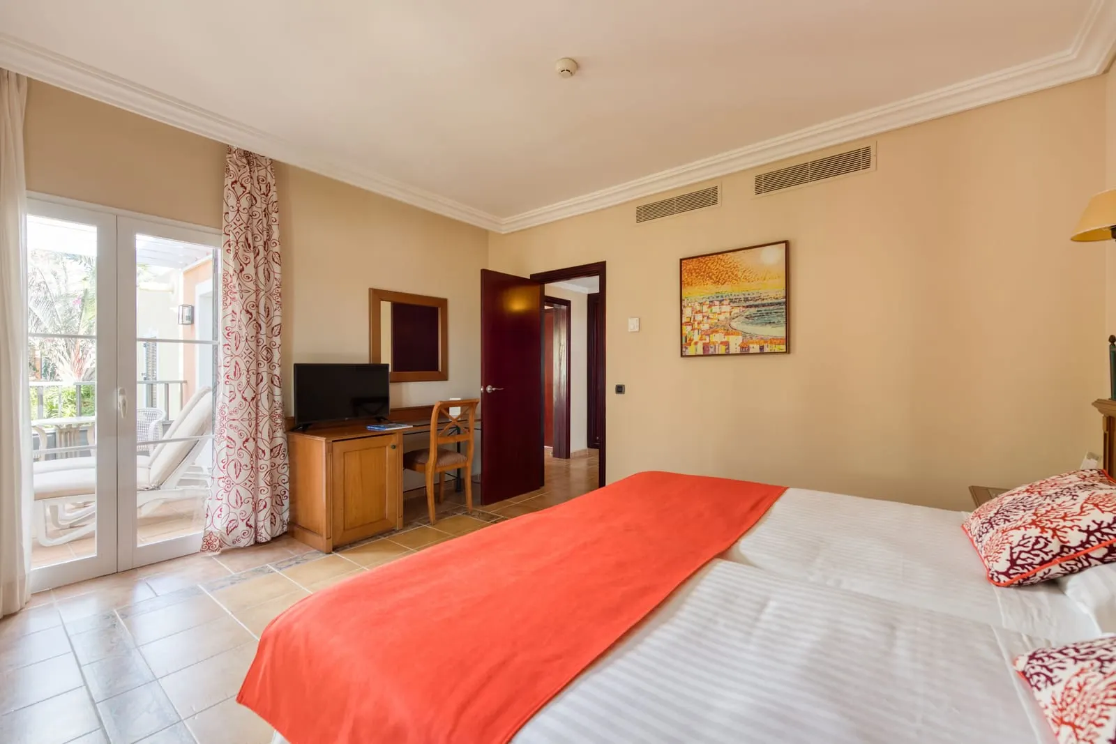 Junior Suite at Hotel Cordial Mogán Playa: the bedroom, with a bed, a desk with a television and glass doors open to a terrace with a sunbed