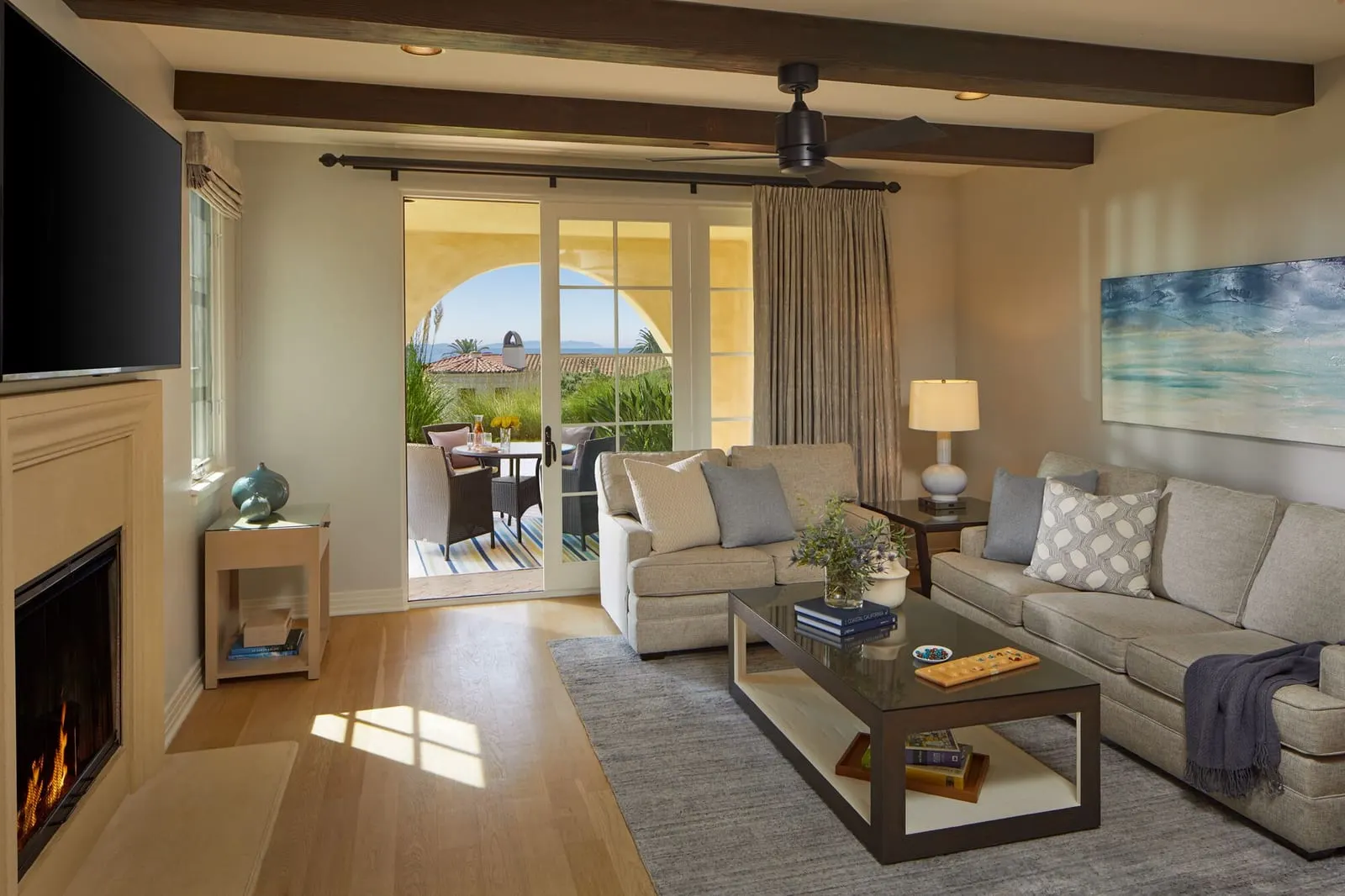 Two-Bedroom Casita, Resort View at Terranea Resort: a living room with a fireplace, a grey sofa and a wall-mounted television under a beamed ceiling, with glass doors to a covered terrace