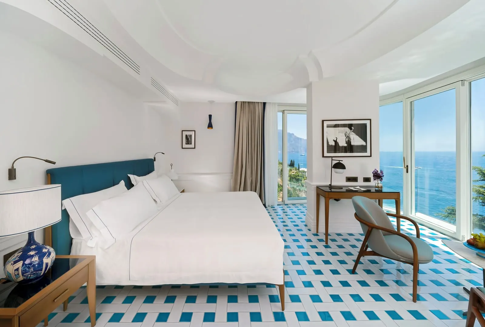 Junior Suite Sea view at Borgo Santandrea: a king bed and a desk with an armchair, and corner windows looking over the sea.