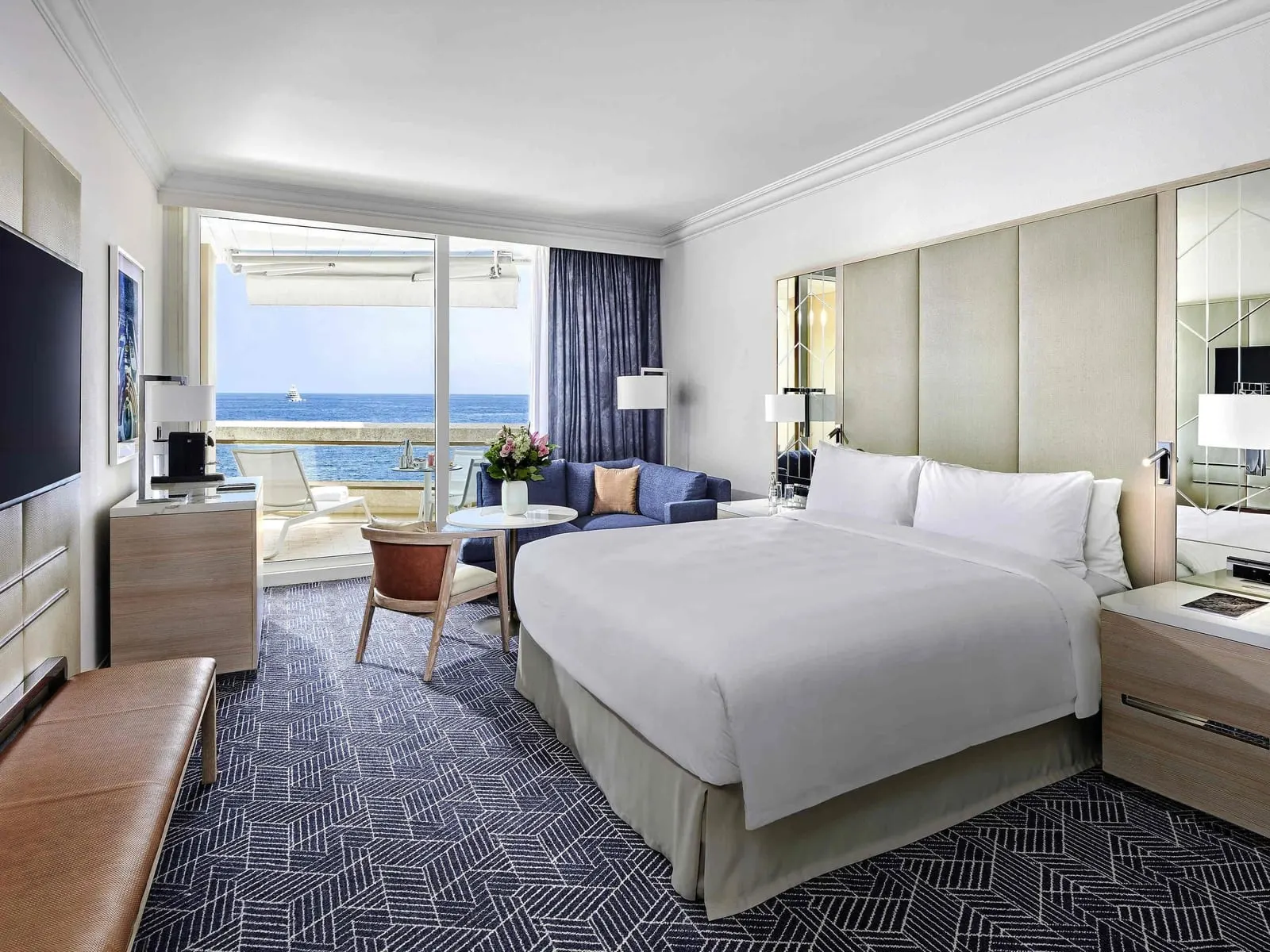 Signature Sea View room at Fairmont Monte Carlo: the bed, a sofa, a desk and glass doors to the terrace and the sea