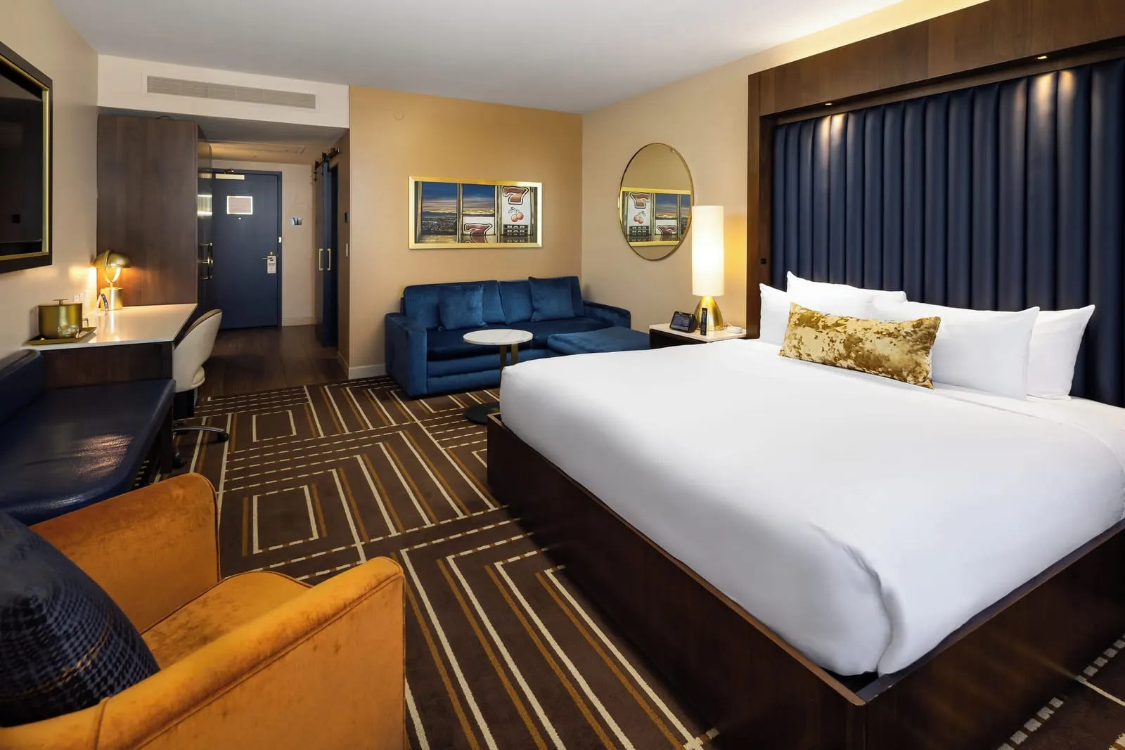 Single King at Circa Resort & Casino: a king bed against a padded blue headboard, a blue sofa with a footstool and a small round table, and an orange armchair in the foreground