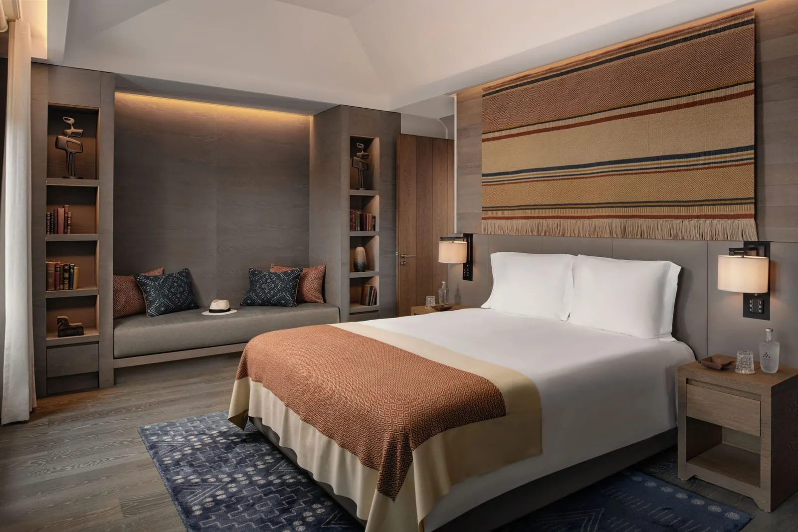 Valley Master Suite at Six Senses Douro Valley: the bed below a large woven hanging, with a cushioned bench in an alcove