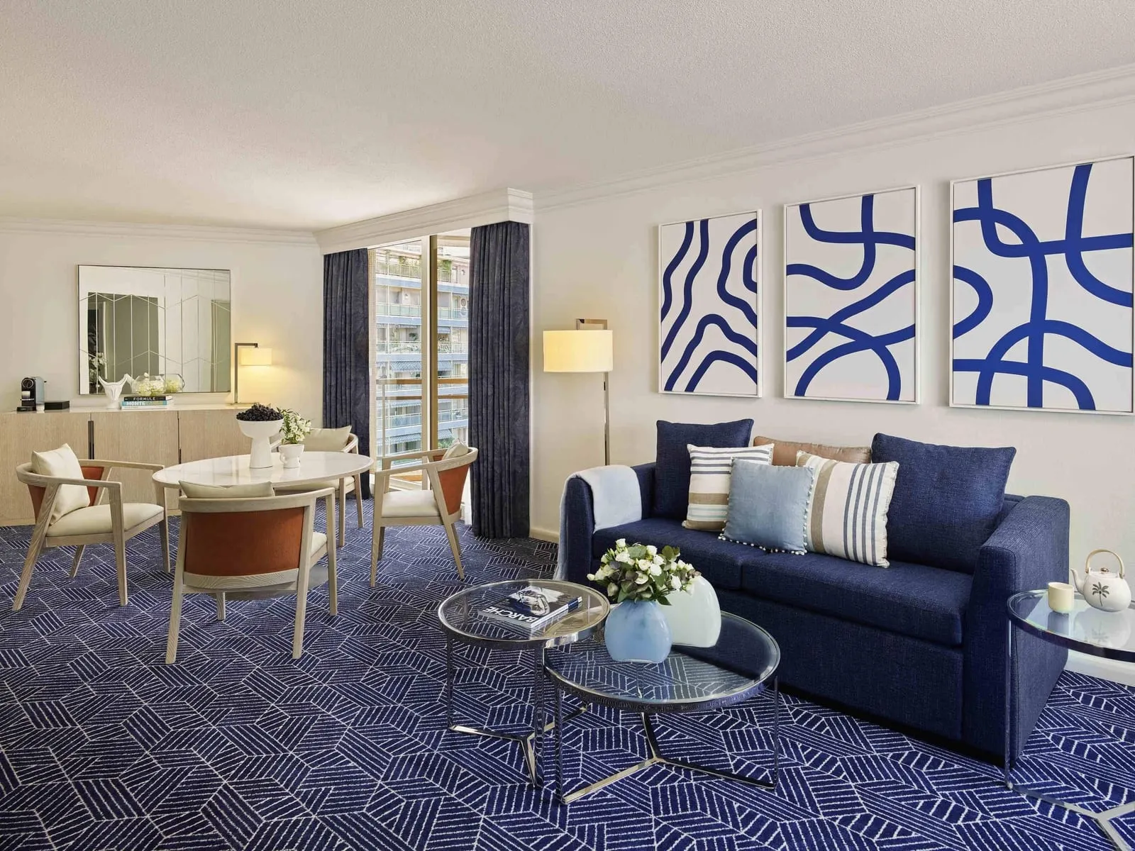 Grand Prix Suite at Fairmont Monte Carlo: the living room with a navy sofa, a dining table and blue artworks