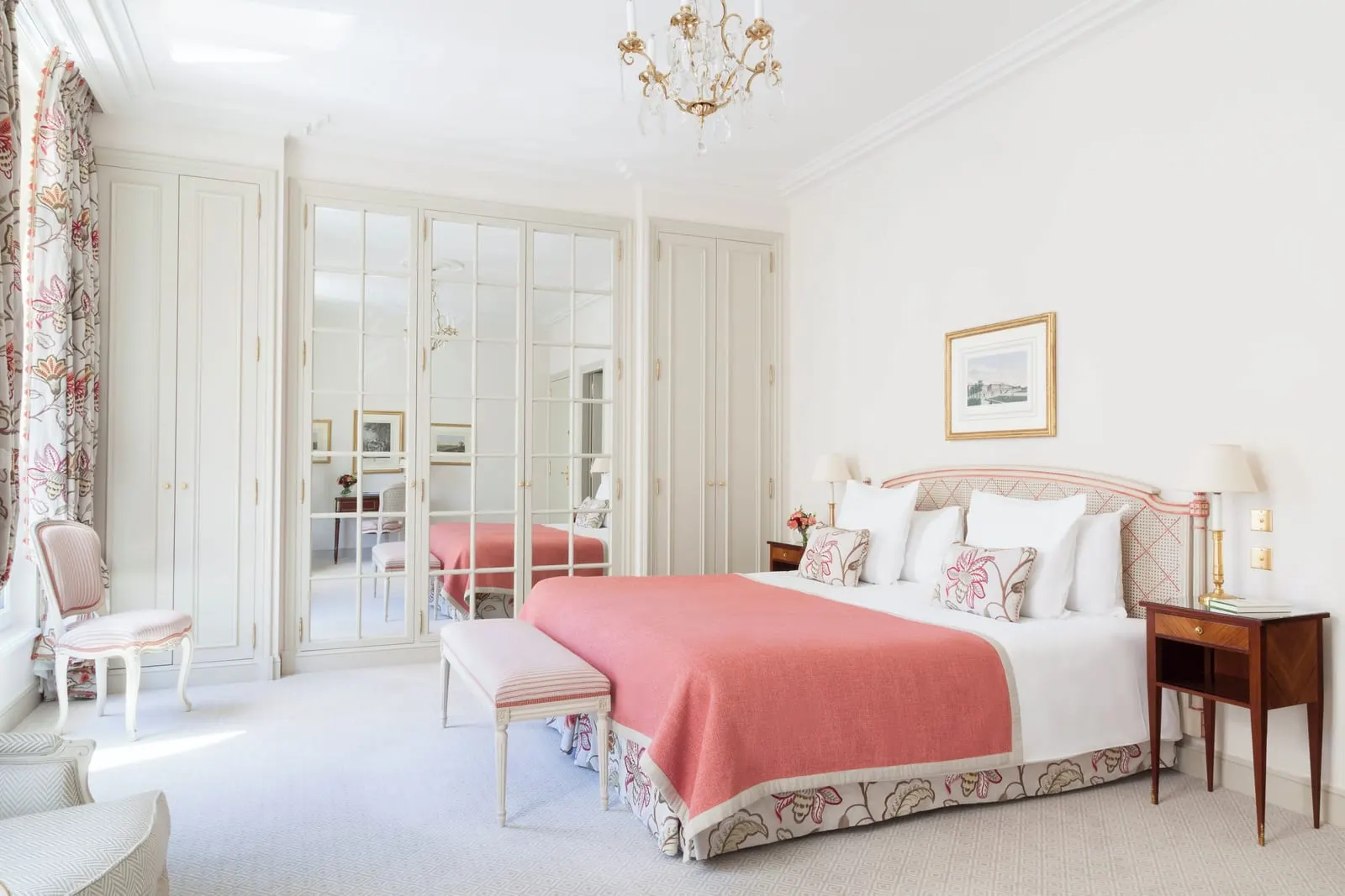 Deluxe Room at Le Bristol Paris: a bed with a coral throw and a cane headboard, a bench at its foot and a wall of mirrored and panelled wardrobe doors