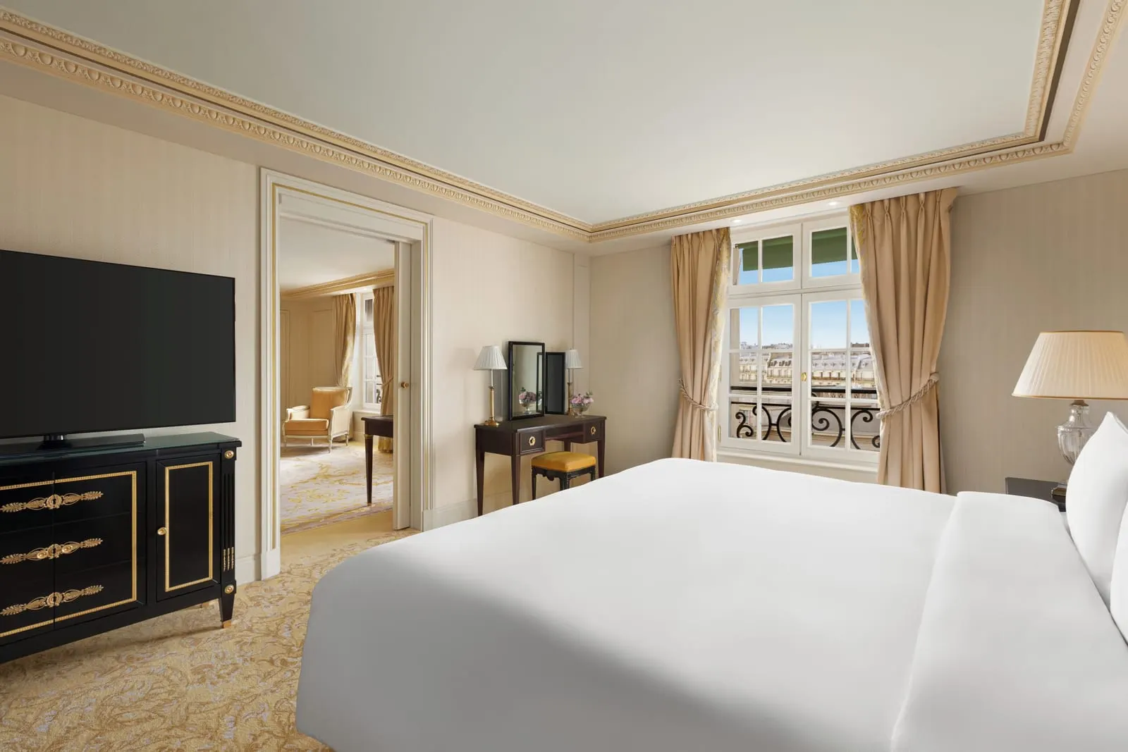 Deluxe Suite at Shangri-La Paris: the bedroom, with a king bed, a dressing table, a black lacquered cabinet under the television and a doorway through to the living room