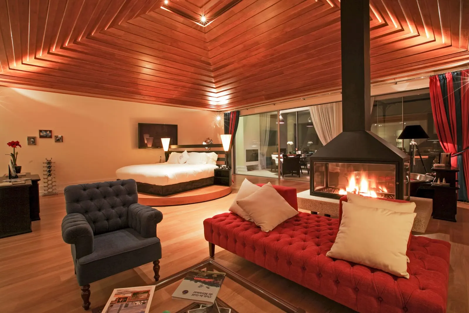 The Bacchus Suite at The Yeatman: a red sofa and armchair by a lit fireplace, with the bed on a round platform beyond