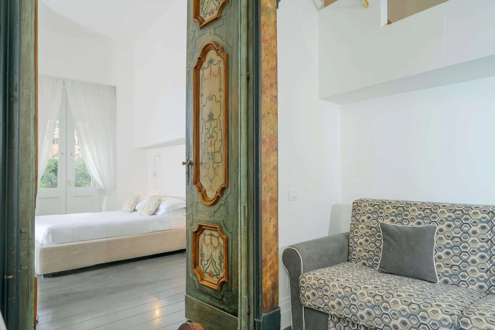 Sea View Presidential Suite im Palazzo Murat: ein Doppelbett, gesehen durch eine bemalte antike Türöffnung, mit einem gemusterten Sofa davor