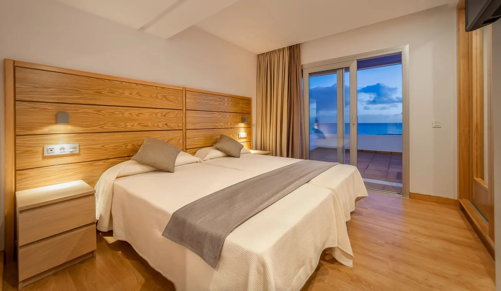 Suite at Hotel Lancelot: a bedroom with two beds under a wood-panelled wall, beside glass doors to the terrace