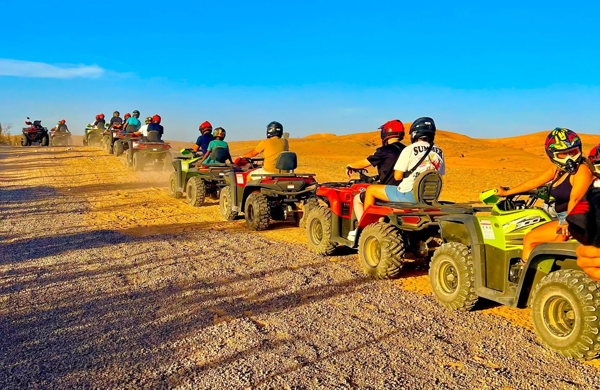 A line of quad bikes with riders in helmets on a stony track through the ochre hills of the Agafay desert