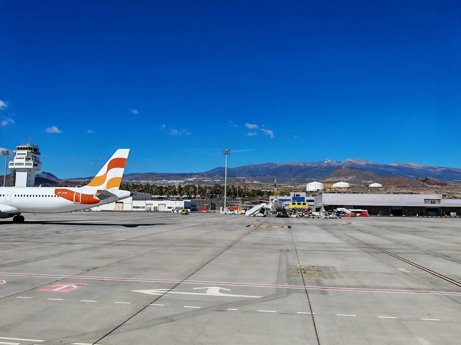 The apron at Tenerife South Airport on a clear day, with the tower and mountains beyond