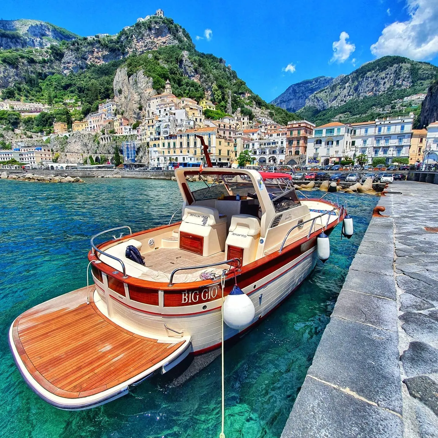 A wooden gozzo moored at the pier in Amalfi, with the town and its cliffs behind