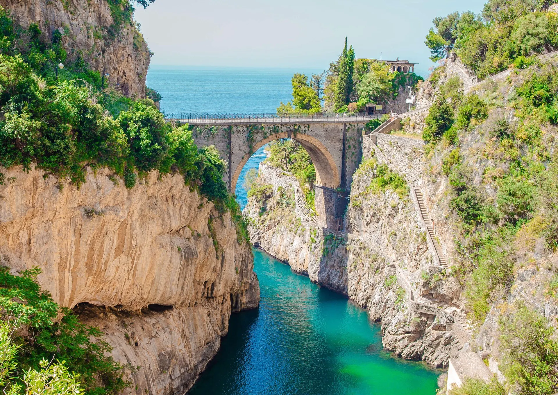 The Furore fjord from above: a narrow inlet of green water between limestone cliffs, crossed by a stone arch bridge
