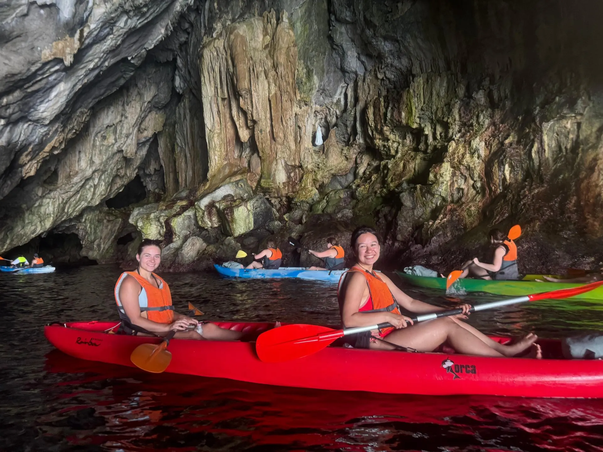 Kayakers in life jackets inside a sea cave hung with stalactites