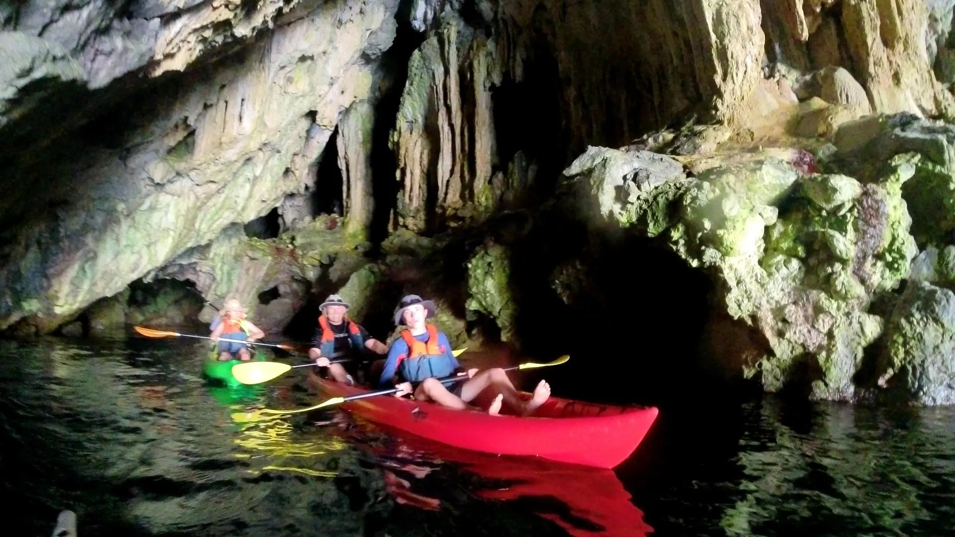 A double kayak and a single kayak on dark water under the rock formations of a sea cave
