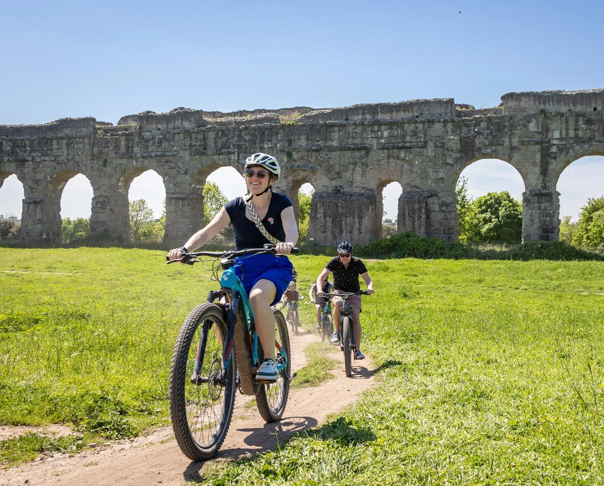 Two riders on e-bikes in front of the arches of the Park of the Aqueducts